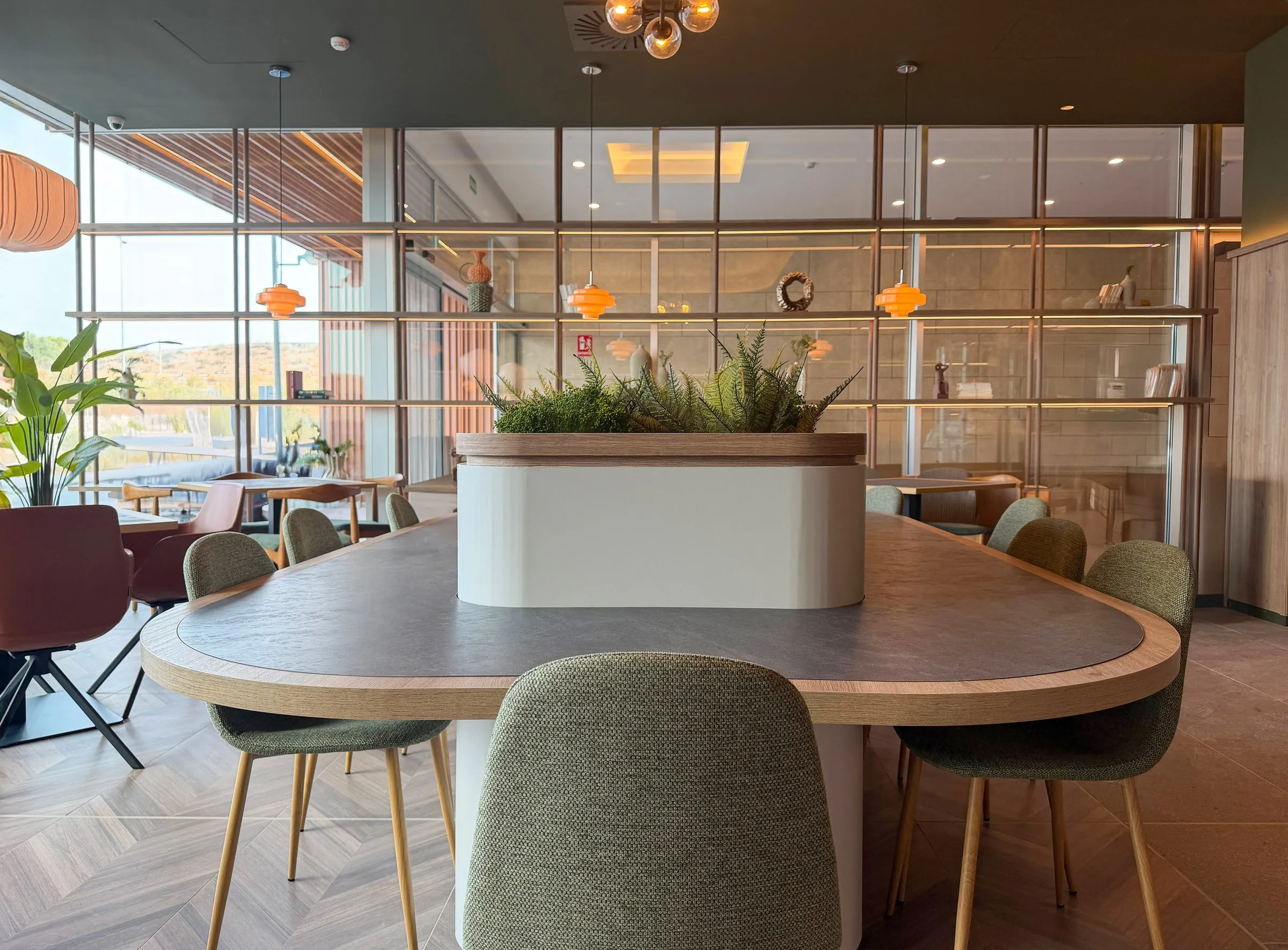 Zona de estar de la recepción del hotel con mesa redonda de madera y cerramiento acristalado
