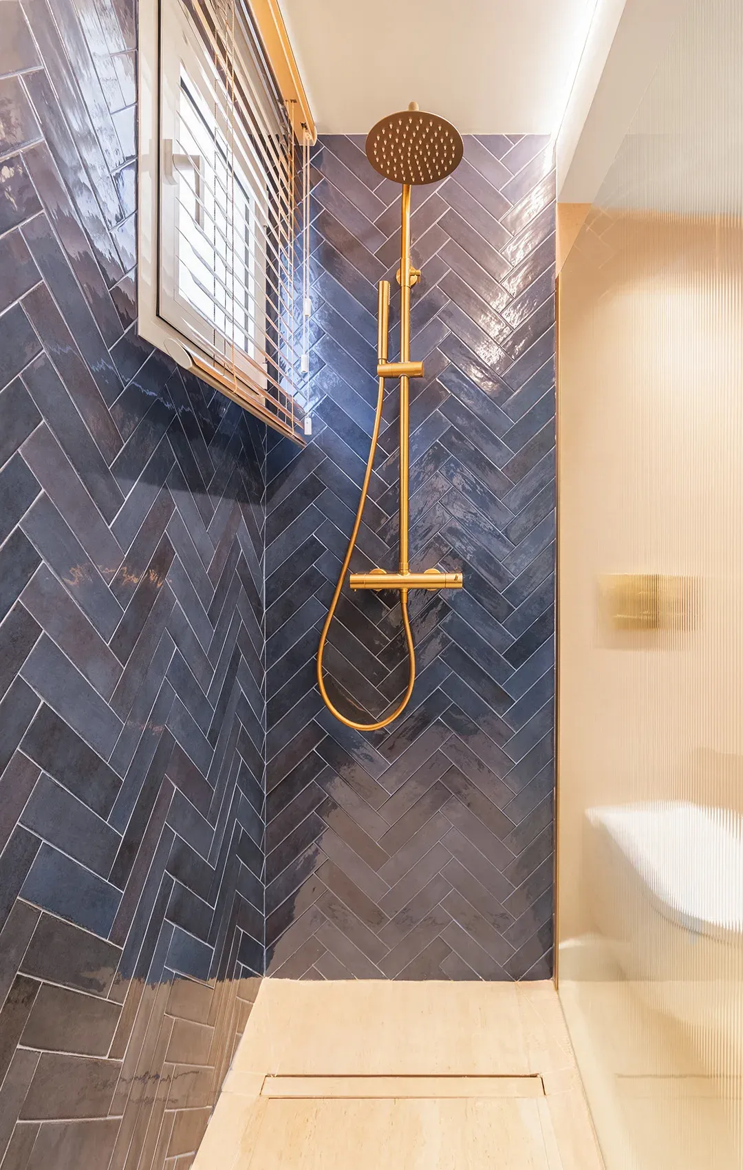 Grifería en tonos dorados de una ducha con azulejos en azul con espiga