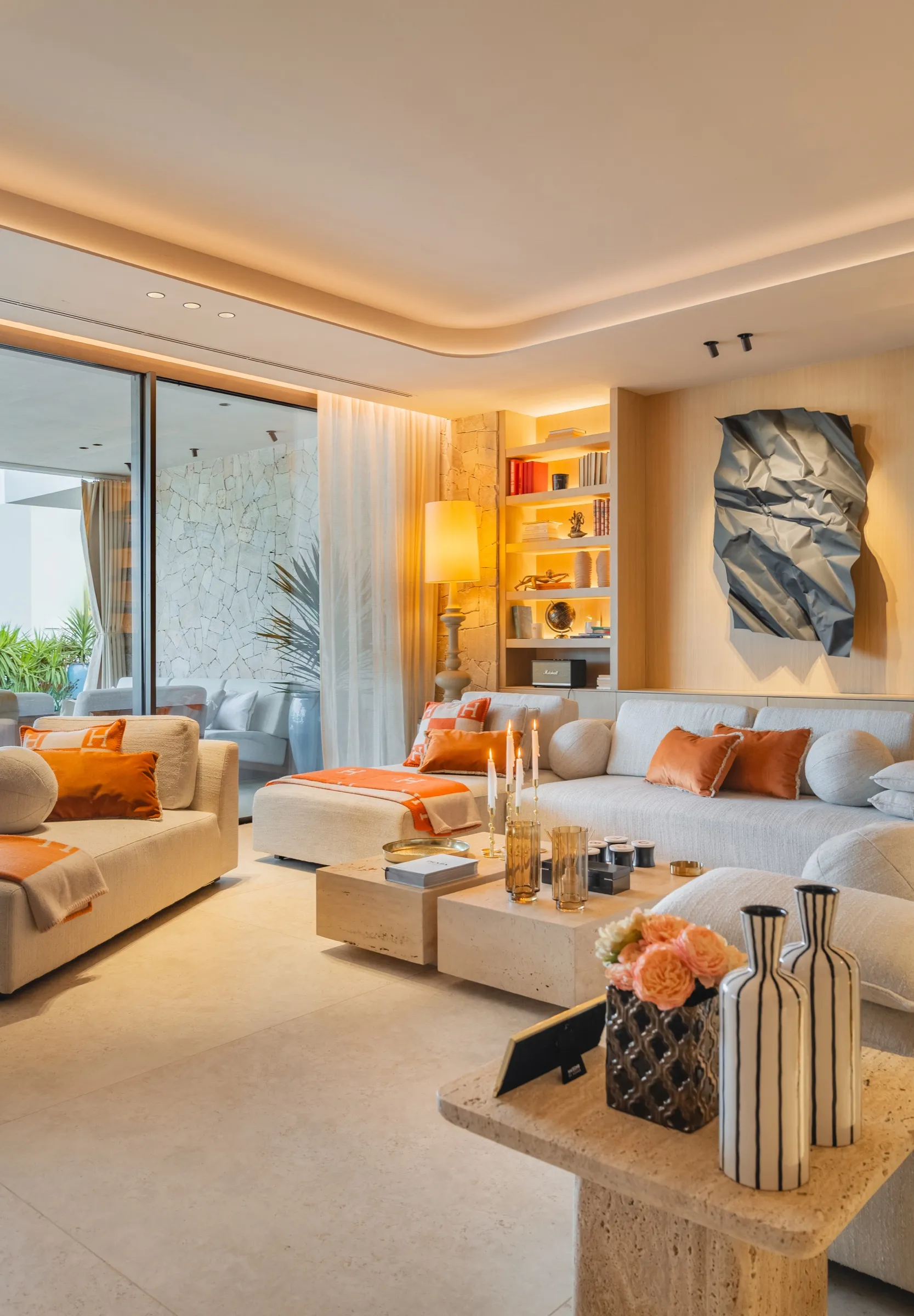 Salón de Villa Möet con sofá blanco, textiles naranjas y librería de roble iluminada
