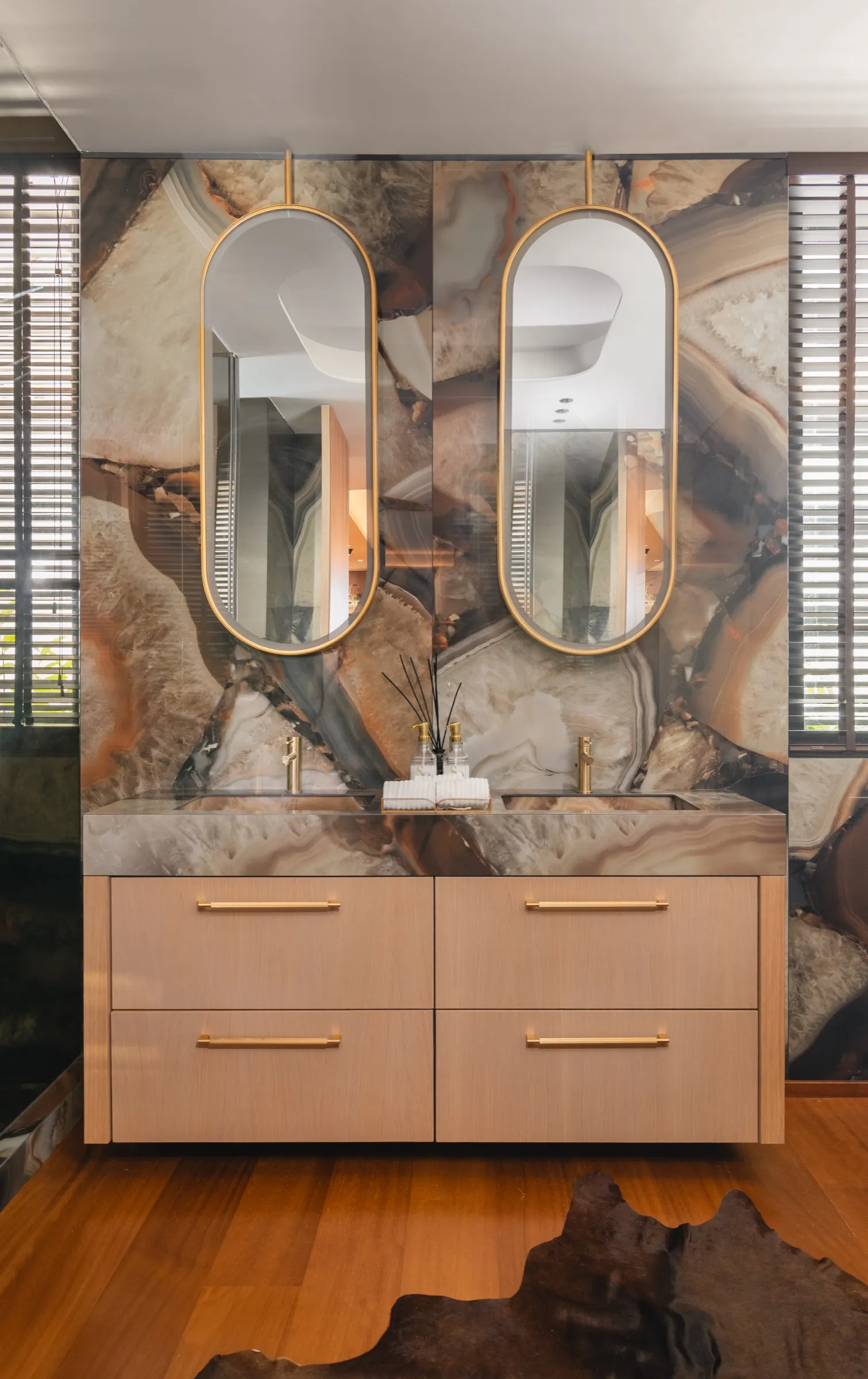 Baño con doble lavabo, espejos ovalados y pared de piedra ágata
