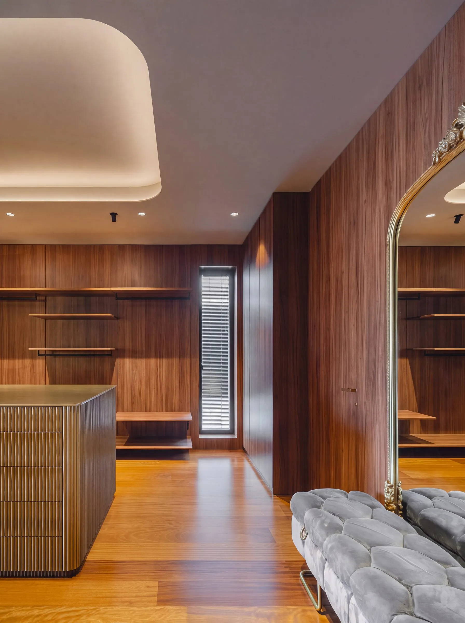 Espejo dorado y banqueta junto al panelado de nogal del vestidor